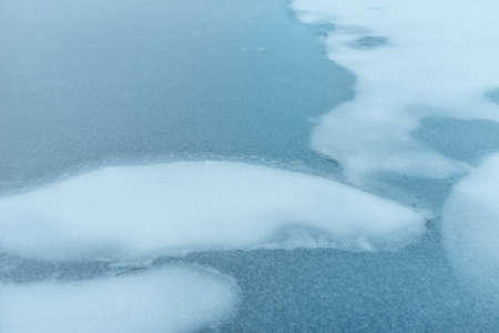 Frozen water.Blue ice frozen lake with snow and cracks at winter. Melting ice on the lake,...