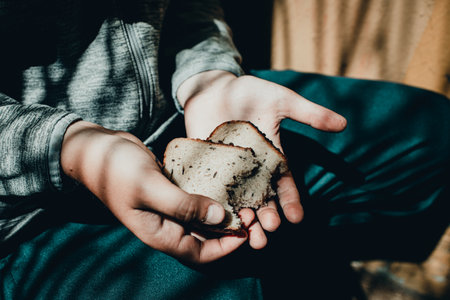 Poor Child homeless, beggar kid holds a pieces of black bread, war concept, poverty, crisis. Selective focus.Close-up.Toned.の写真素材