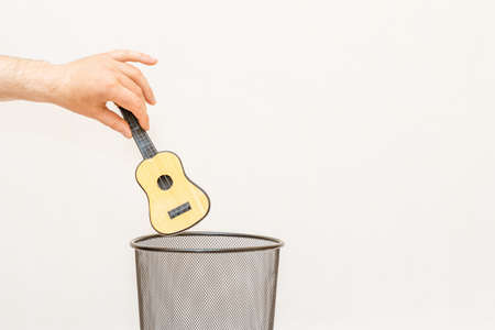 The small toy guitar is thrown into the trash,can for disposal and recycling.White,gray background,selective focus,copy space.の写真素材
