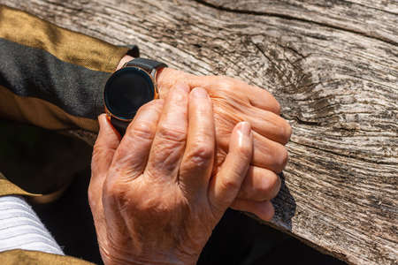 Elderly woman with smart watch fitness band checking her pulse,outdoors on the old wooden...
