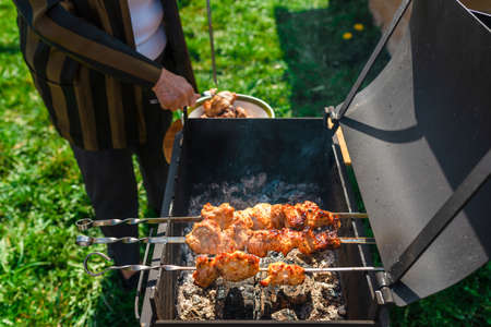 Senior woman doing process of cooking barbecue completed on a metal grill.Cooking for a picnic.Delicious, juicy, aromatic pieces of shashlik.Meadow background.の写真素材