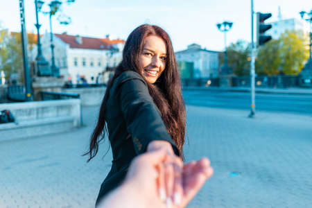 Happy brunette girl with a smile on her face holding boyfriend's hand on a street at sunset on a warm spring,summer evening.Follow-me concept.Selective focus.の写真素材