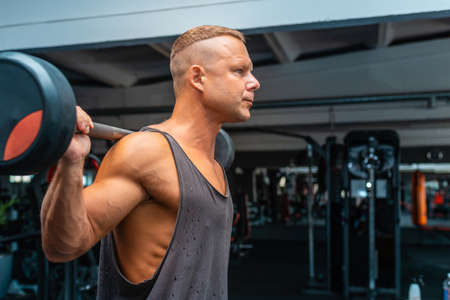 Fit young caucasian man lifting barbell, focused on weight, working out in a gym.Side view,copy space.の写真素材