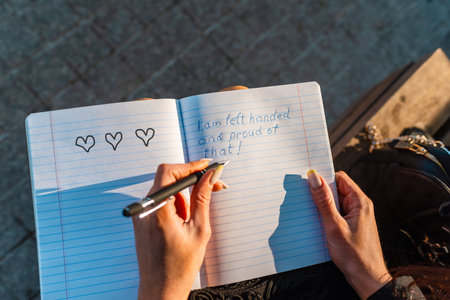Woman writes in a notebook, holding pen in her left hand.Outdoors summer evening park. Left-handers...