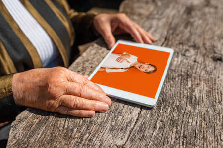 Happy elderly woman holding tablet pc computer looking at her granddaughter photo album at home.Technology,age,memories and people concept.Close up.の写真素材