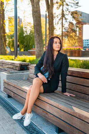 Beautiful and elegant business woman sitting in a park.Summer sunset portrait of a charming caucasian lady.の写真素材