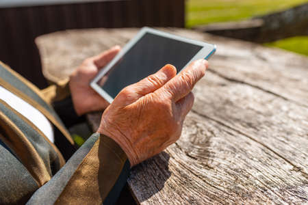 Hands of senior woman holding tablet PC, outdoors in warm summer day.Close up.Selective focus.