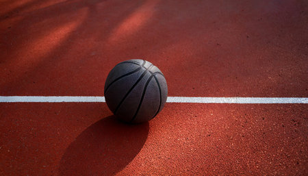 Black Basketball ball is sitting in the red rubber court vertical white line outdoors, top view. copy space.image for sport, exercise concept.High quality image.の素材