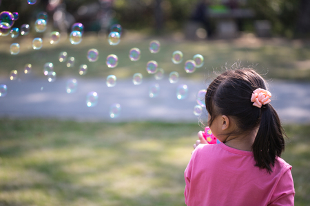 Little girl blowing bubbles under the sunの写真素材