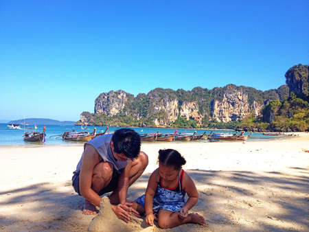 Dad and daughter playing sand in the beachの素材