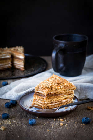 Slice of homemade medovik layered honey cake, traditional russian cake with cream and caramel on plate on rustic wooden table. Vertical composition, selective focus, warm toneの写真素材