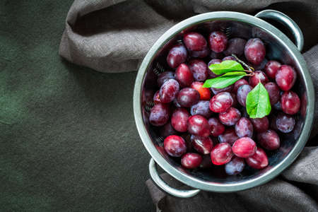 Group of fresh red plums in silver bowl, top view with copy space on backgroundの写真素材