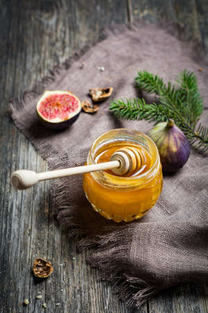 Jar of honey, fresh figs and walnuts on rustic wooden table. Christmas food still life, selective focus, natural light, toned imageの写真素材