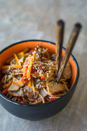 Stir fry with vegetables and meat garnished with sesame seeds in bowl with chopsticks. Traditional asian cuisineの写真素材