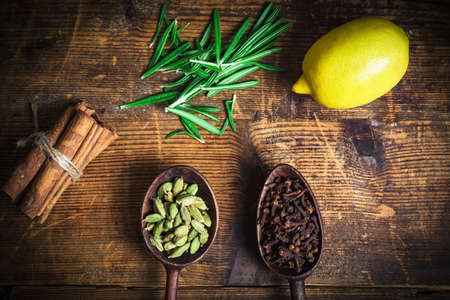 Spices culinary condiments on wooden table: cloves, cinnamon sticks, cardamom pods and rosemary. Table top viewの写真素材