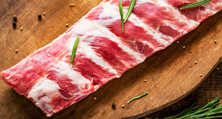 Pork ribs with spices uncooked on wooden cutting board. Rusty style, high contrast. Close upの写真素材
