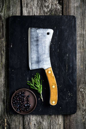 Cutting board, meat cleaver and condiments on dark wooden background. Cooking ingredients. Copy spaceの写真素材