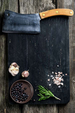 Old cleaver butcher meat knife and spices on wooden cutting board, texture background. Cooking ingredients. Copy space. Mock up for cook bookの写真素材