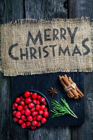 Merry Christmas greeting on linen material decorated with cinnamon sticks, star anise, rosemary and...