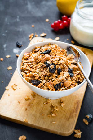 Homemade granola with nuts and dried fruits in white bowl, jar of fresh yogurt and fruits on wooden backgroundの写真素材