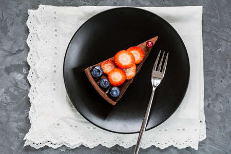 Chocolate tart topped with fruits and berries on black plate, top viewの写真素材
