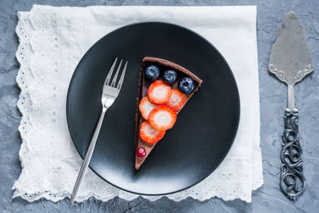 Chocolate tart topped with fruits and berries on black plate, top viewの写真素材