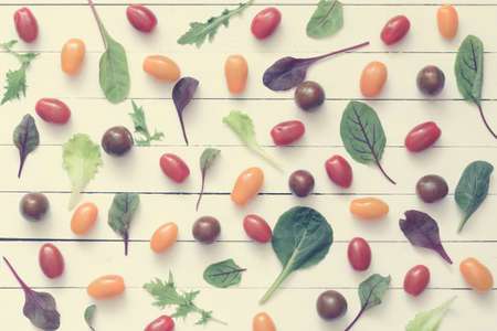 Cherry tomatoes and green salad leaves on white wooden background. Top view, flat lay food. Vintage toningの写真素材
