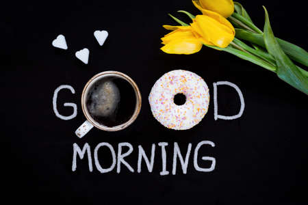 Donut, cup of coffee, flower yellow tulip and heart shaped sugar cubes. Good morning greeting on black chalk board. Top viewの写真素材