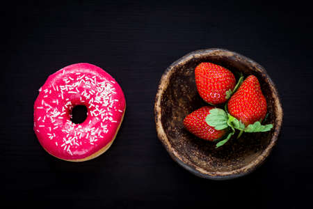 Fresh strawberries in bowl and sweet glazed pink donut on black background. Top viewの写真素材