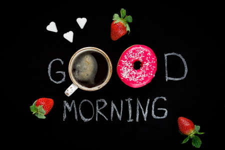 Donuts and strawberries. Good morning greeting written on black chalk board. Table top view....