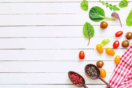 Fresh cherry tomatoes, salad leaves and spices on white wooden background with copy space. Healthy cooking background, good for menu, recipe or web sites banner.の写真素材