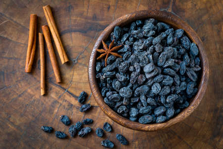 Black raisins in wooden bowl. Cinnamon sticks on side. Top view, close up, horizontalの写真素材