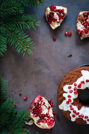 Chocolate bundt cake with cream cheese glaze and pomegranate seeds, fresh pomegranate and fir tree branches creating frame. Copy space for text.の写真素材