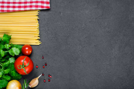 Italian cuisine cooking ingredients: dry pasta, spices and vegetables on slate background with copy space for textの写真素材