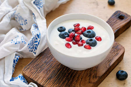 Fresh yogurt with blueberries and pomegranate seeds in white bowl