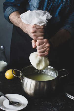 Process of making cheese: man squeezing cheesecloth to extract whey. Vertical composition, toned image.の写真素材