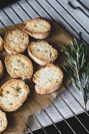 Crostini with rosemary olive oil on parchment paper on cooling rack. Selective focus, vertical composition, desaturated colors.の写真素材