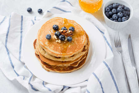 Stack of pancakes with fresh blueberries, nuts and honey on white plate. Healthy breakfast food.の写真素材