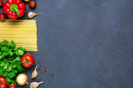Pasta, spices and vegetables on slate background - cooking ingredients for italian cuisine. Copy space for test. Horizontal, top view.の写真素材