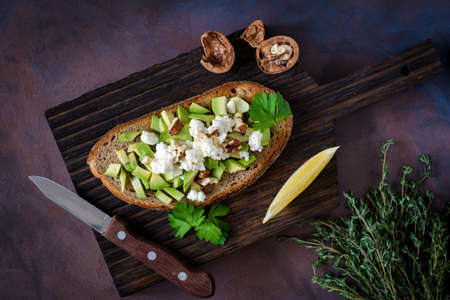 Avocado, cheese and walnuts salad on toasted bread, served on wooden cutting board with lemon wedge. Healthy snackの写真素材