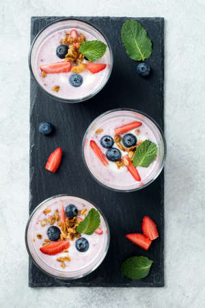 Purple blueberry fruit smoothies decorated with fresh berries, granola and mint on slate background....