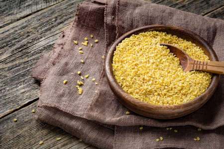 Uncooked bulgur in wooden bowl on wooden table background, rustic style. Bulgur wheat grainsの写真素材