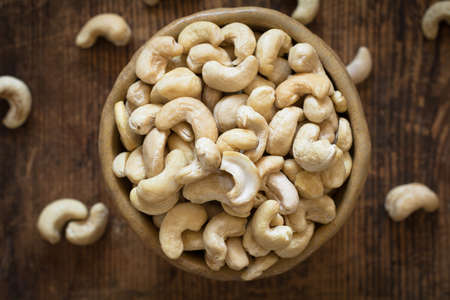 Raw cashew nuts in bowl on textured wooden background, table top view, selective focus