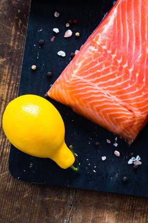 Raw salmon fillet, lemon and spices on black board, textured wooden backgroundの写真素材