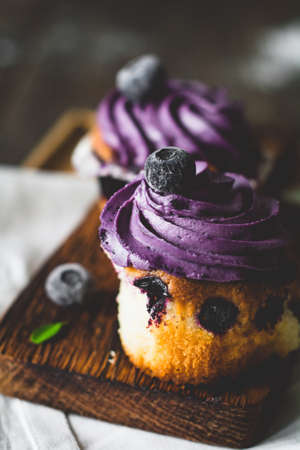 Blueberry cupcakes with purple butter cream on wooden board, close upの写真素材