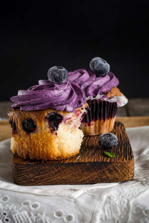 Blueberry cupcakes with purple butter cream on wooden board, close upの写真素材