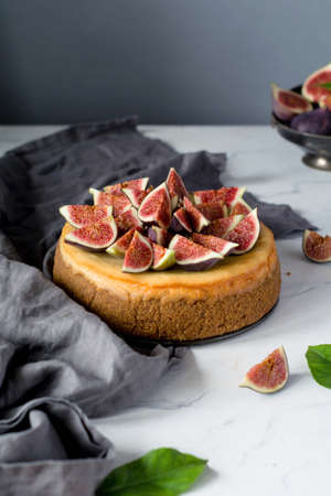 Whole cheesecake decorated with fresh figs on a marble table. Vertical view, copy space for textの写真素材