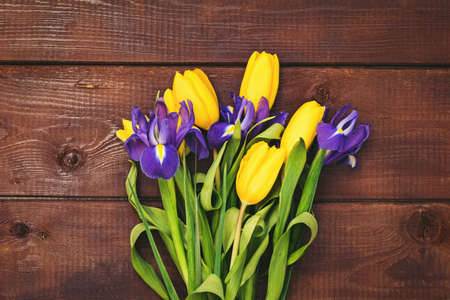 Bouquet of flowers. Yellow tulips and iris flowers over brown wooden background. Table top view and copy space for text. Holidays, Easter, Mother's day background or cardの写真素材