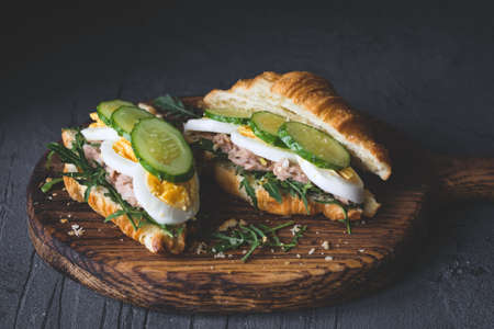 Tuna salad sandwich with boiled egg, arugula, cucumber and tuna salad on wooden cutting board. Closeup view, selective focus, toned imageの写真素材