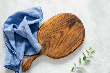 Wooden cutting board for cooking, blue kitchen napkin and olive branch on a gray stone background. Top view, copy space for textの写真素材